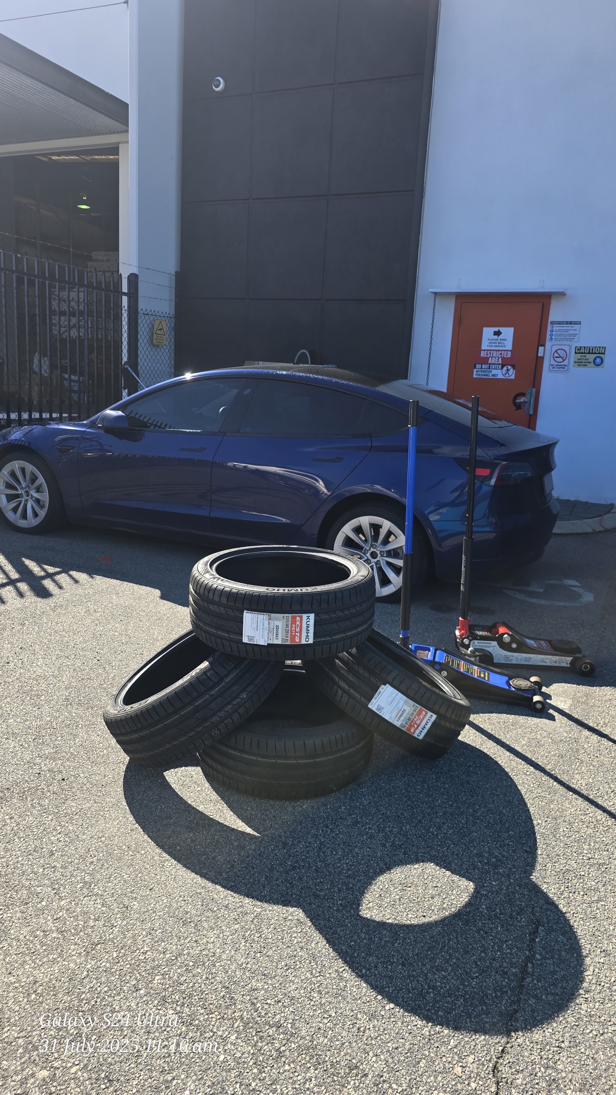 A stack of new tyres ready to fit at a customer's premises, with the customer's Tesla behind
